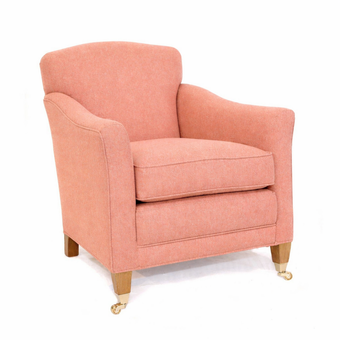 Macey armchair upholstered in coral pink fabric with light wooden legs and brass castor feet