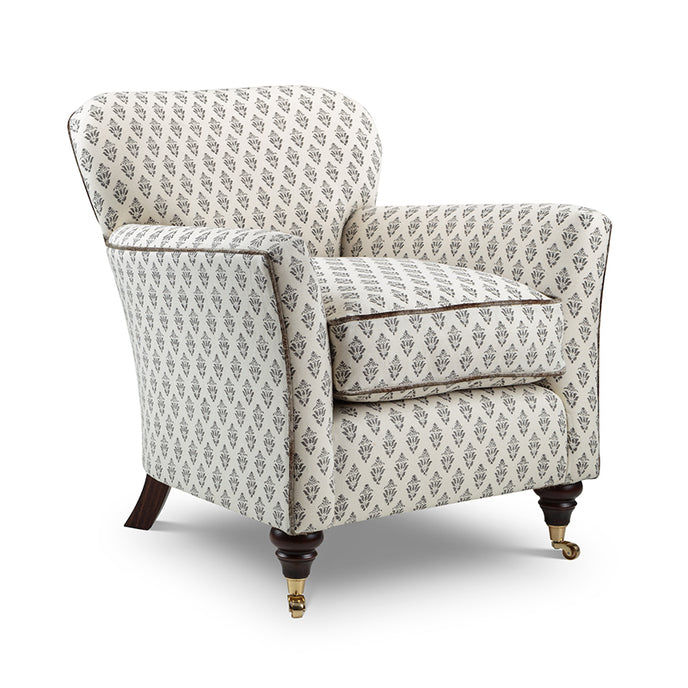 Lucia armchair upholstered in beige and grey patterned fabric with dark wooden legs and brass castors