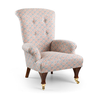 Newbury Chair upholstered in pink and blue geometric patterned fabric with a high button-tufted back, rolled arms, and wooden legs with brass castors