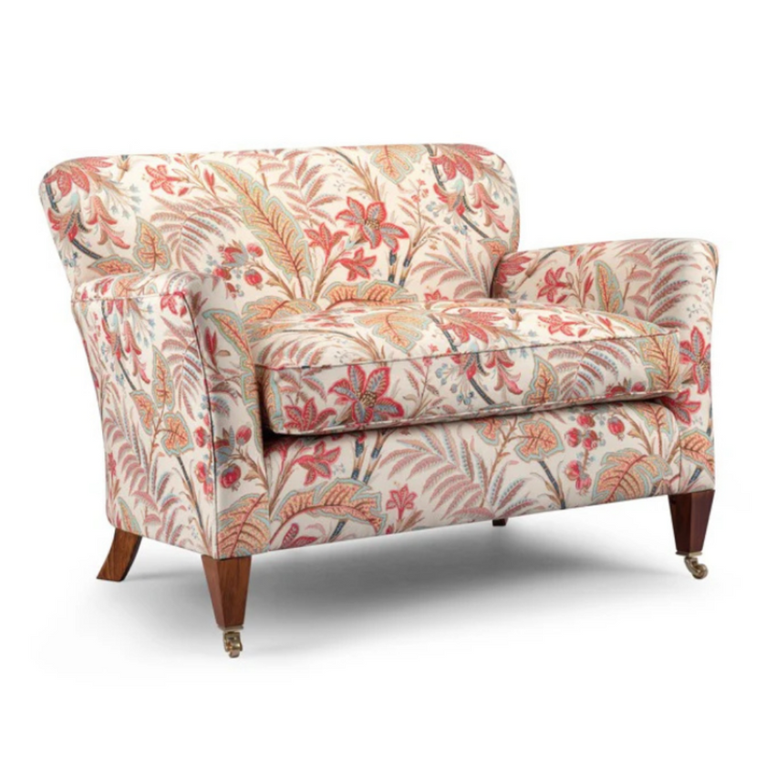 Lucia Sofa upholstered in cream floral fabric with tapered wooden legs and brass castors